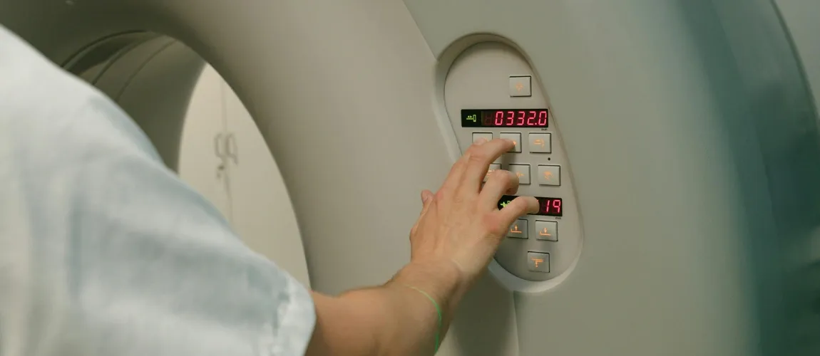 Eine Person drückt einen Knopf an einem Computertomographen.