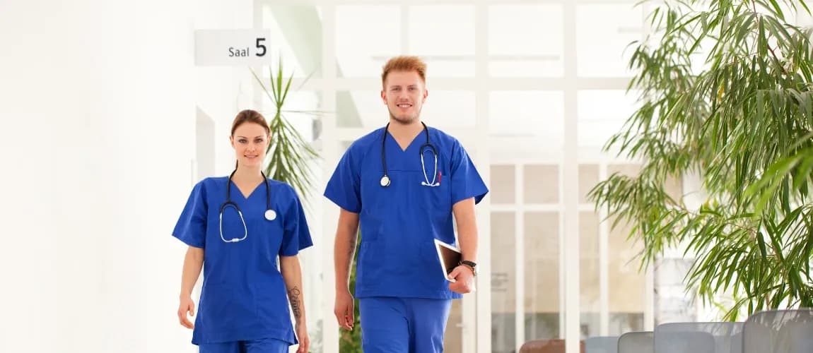 Zwei Pflegekräfte laufen nebeneinander durch ein Krankenhaus. 