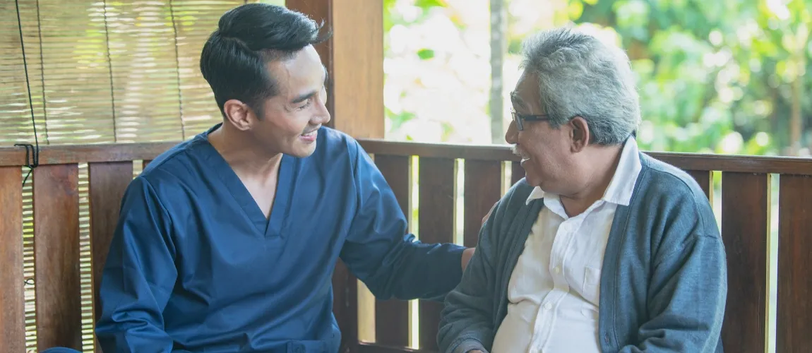 Ein Senior sitzt mit einer Pflegefachkraft auf einer Veranda.