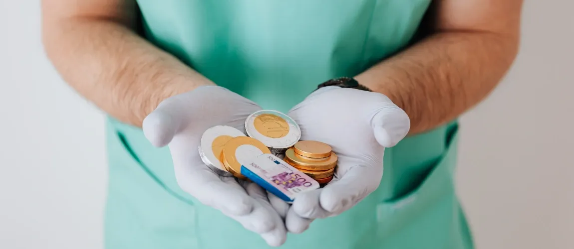 Eine Person in Pflegekleidung hält Geld in ihren behandschuhten Händen.