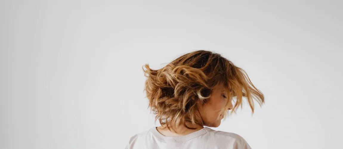 Eine Frau in einem weißen Oberteil schüttelt ihr Haar.