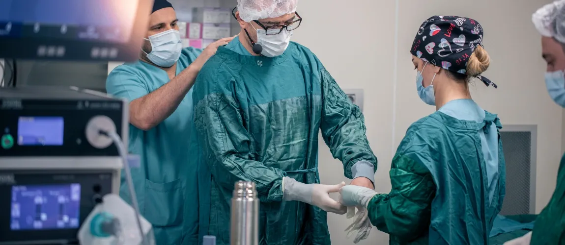 Zwei Personen legen bei einem Mediziner OP-Kleidung an. 