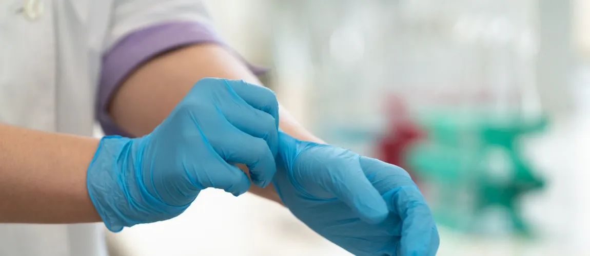 Eine Person zieht sich blaue Einmalhandschuhe an.
