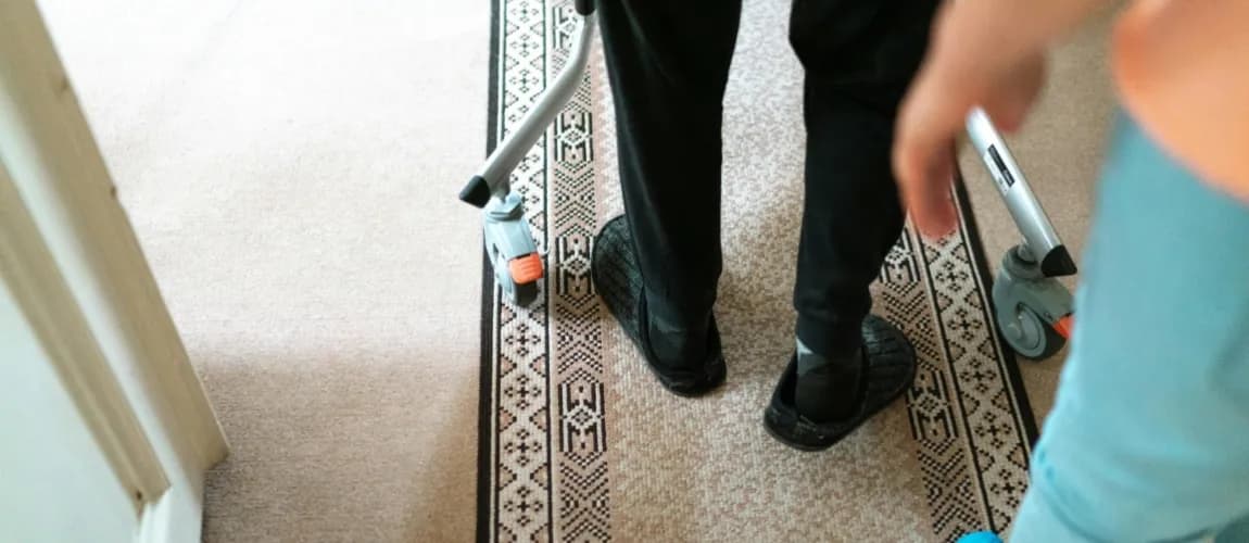 Fokus auf zwei Menschen, die einen Gang entlang gehen, eine Person hat ein Hilfsmittel.