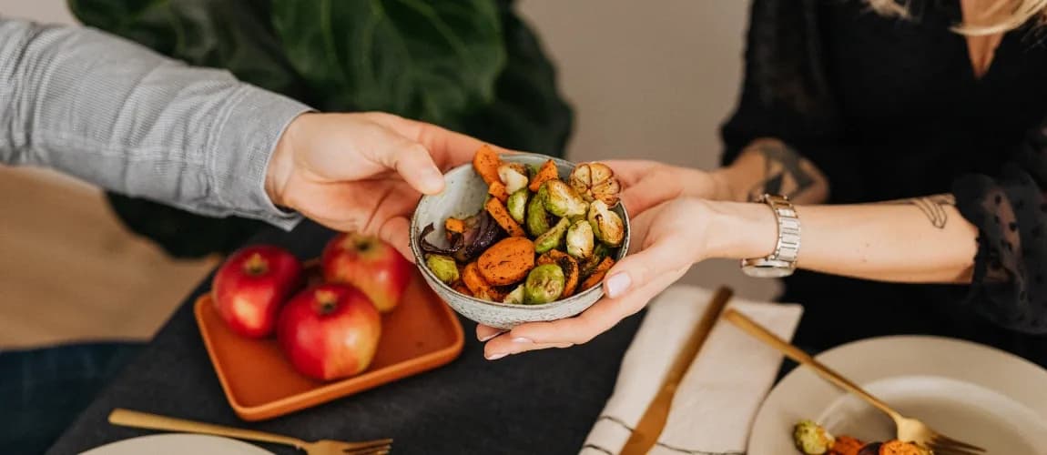 Ein Mann reicht einer Frau eine Schüssel mit zubereitetem Gemüse. 
