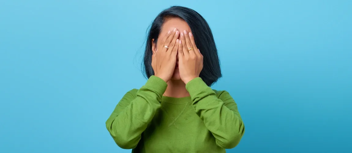 Eine Frau in einem grünen Pullover hält sich die Augen zu.