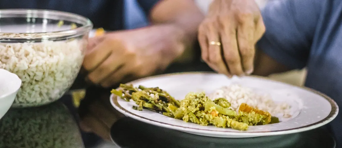 Eine ältere Person greift nach einem Teller mit Reis und Gemüse.
