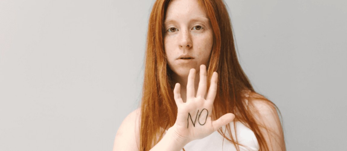 Eine rothaarige Frau hält die Hand die Kamera, darauf steht "NO" geschrieben.