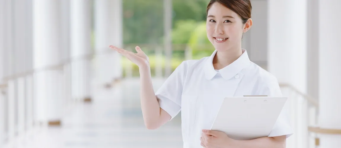 Eine Frau in einem weißen Oberteil steht auf einem Gang und hält eine Hand hoch.