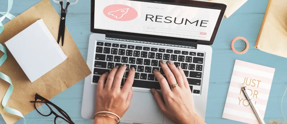 Eine Frau tippt auf einem Laptop, daneben liegen Büromaterialien.