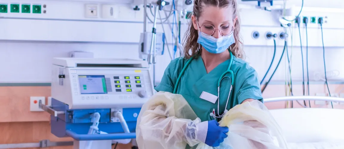 Eine Pflegekraft zieht sich Schutzkleidung an.