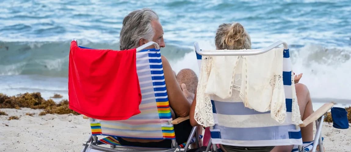 Ein Senior und eine Seniorin sitzen auf Stühlen am Strand.