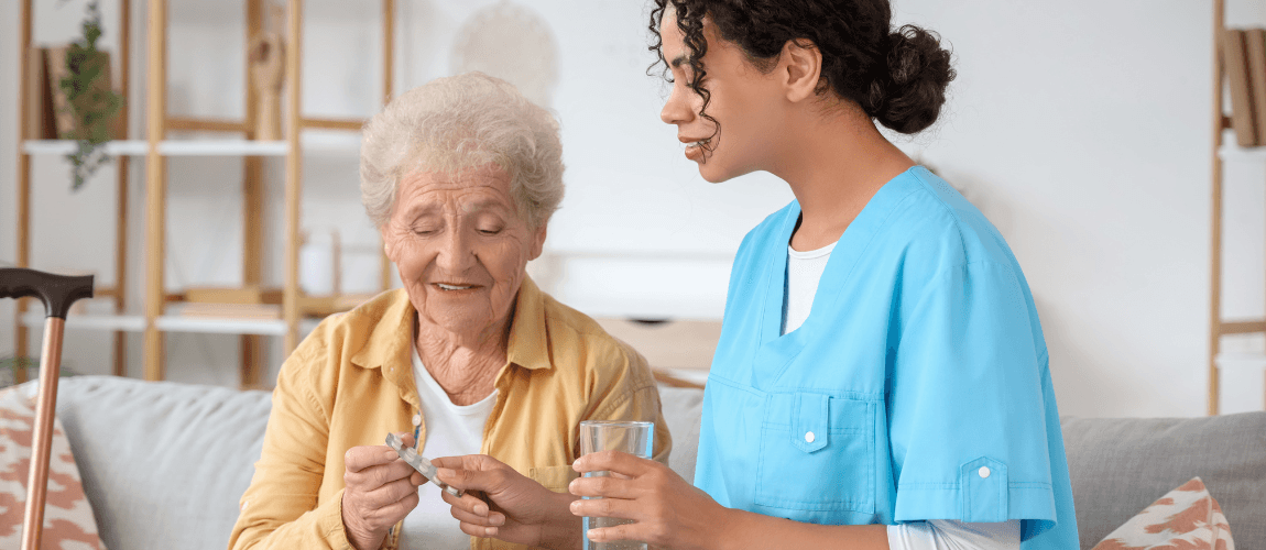 Eine Pflegekraft reicht einer älteren Patientin Medikamente an.
