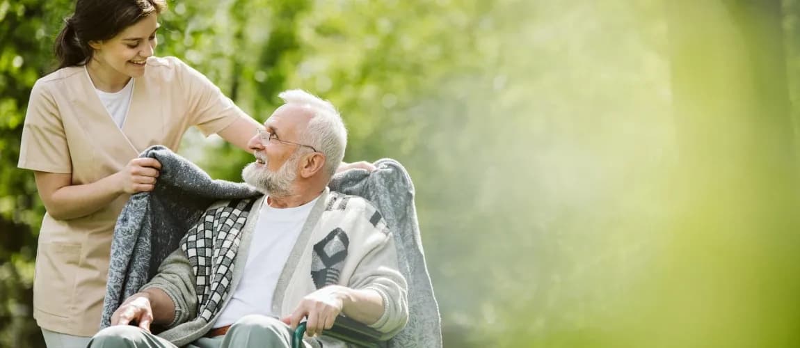 Eine Pflegeperson hilft einem Pflegebedürftigen im Rollstuhl.